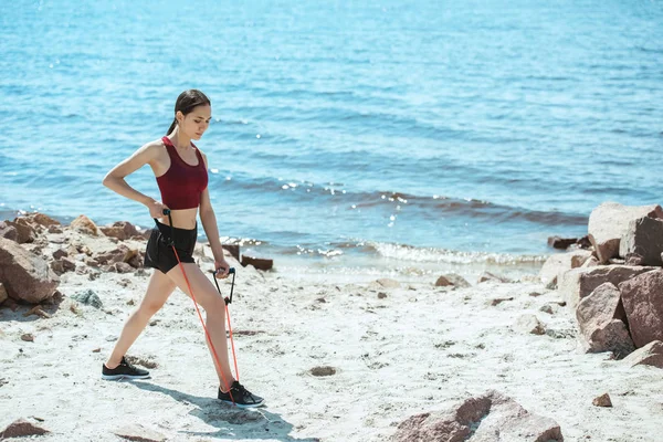 Junge Sportlerin turnt mit Stretchband am Strand — Stockfoto