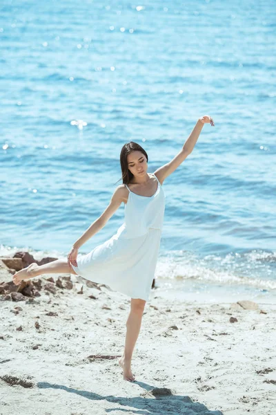 Focalisé asiatique femme en blanc robe danse sur plage par mer — Photo de stock