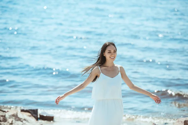 Счастливая женщина в белом платье с широкими объятиями стоит у моря — стоковое фото
