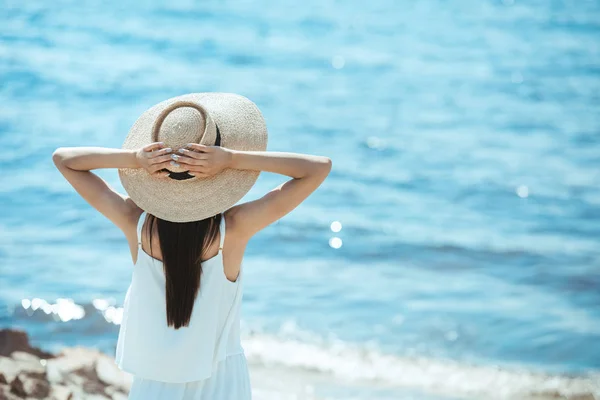 Rear view of woman in white dress and straw hat standing in front of sea — Stock Photo