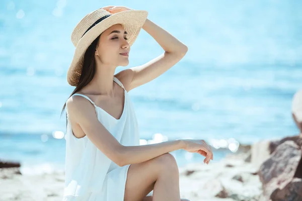 Smiling asian woman in straw hat and white dress by sea — Stock Photo