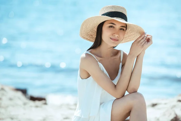Селективный фокус привлекательной азиатской женщины в соломенной шляпе на пляже — стоковое фото