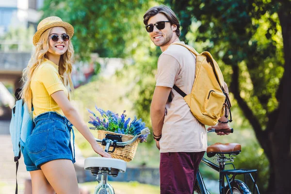 Vista trasera de la joven pareja sonriente con mochilas y bicicletas en el parque - foto de stock