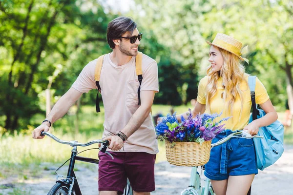 Jeune couple souriant avec sacs à dos et vélos dans le parc — Photo de stock