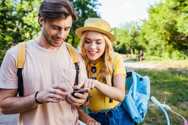 Retrato de pareja sonriente usando teléfono inteligente en el parque en el día de verano - foto de stock