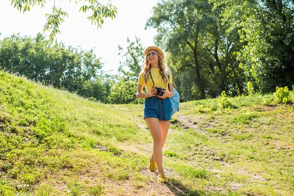 Jeune femme souriante en chapeau avec appareil photo marche dans le parc d'été — Photo de stock