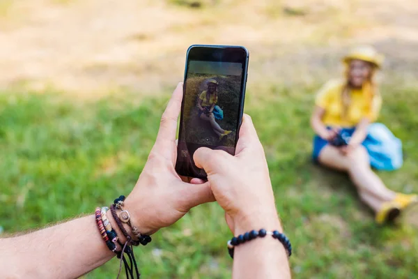 Vue partielle de l'homme prenant une photo de petite amie sur la pelouse verte dans le parc — Photo de stock