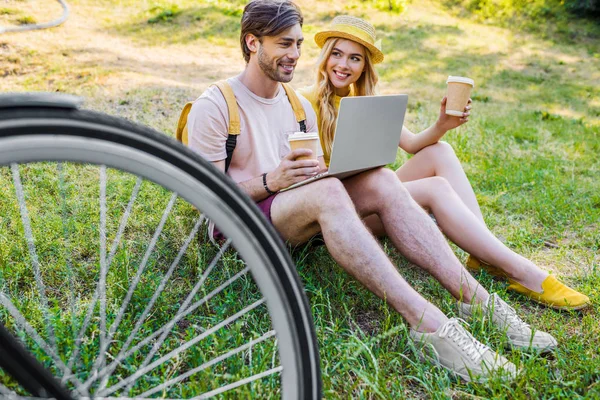 Pareja joven con café para ir con el ordenador portátil en el parque - foto de stock