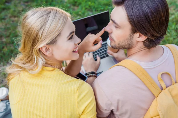 Vue arrière du couple souriant avec ordinateur portable et smartphone reposant sur l'herbe verte dans le parc — Photo de stock