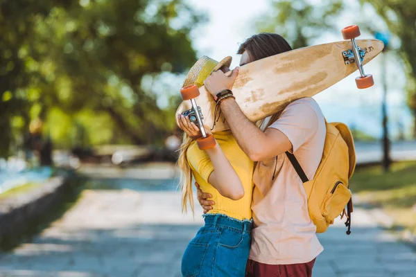 Obscured view of couple kissing behind longboard in hands — Stock Photo