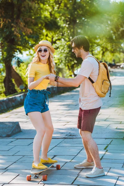 Hombre ayudando novia patinaje en longboard en la calle - foto de stock