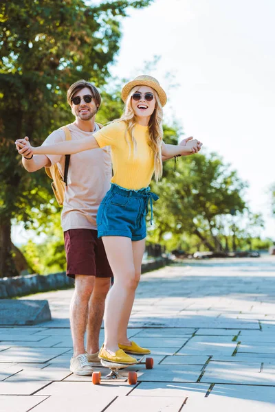 Man helping girlfriend skating on longboard on street — Stock Photo