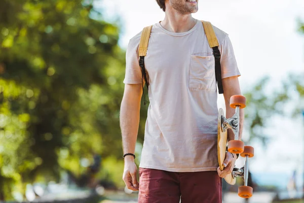 Vista parcial del hombre con mochila y longboard caminando por la calle - foto de stock