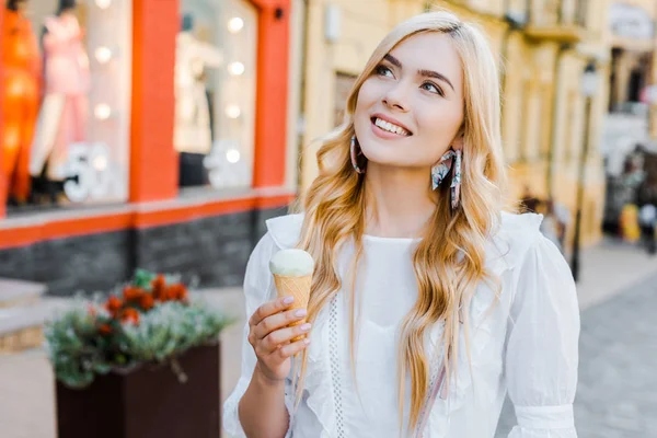 Portrait de belle femme souriante avec crème glacée à la main regardant loin dans la rue — Photo de stock