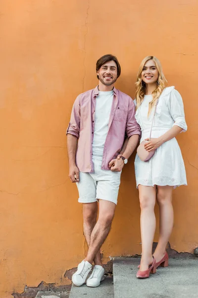 Young stylish couple holding hands while standing against city building wall — Stock Photo