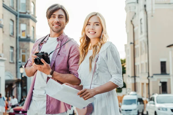 Portrait of smiling tourists with map and photo camera on city street — Stock Photo