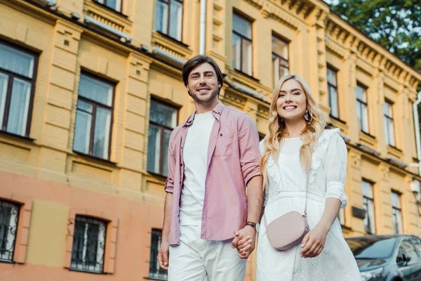 Jeune couple tenant la main tout en marchant sur la rue de la ville ensemble — Photo de stock