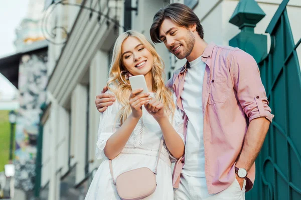 Retrato de casal jovem sorrindo usando smartphone juntos na rua — Fotografia de Stock