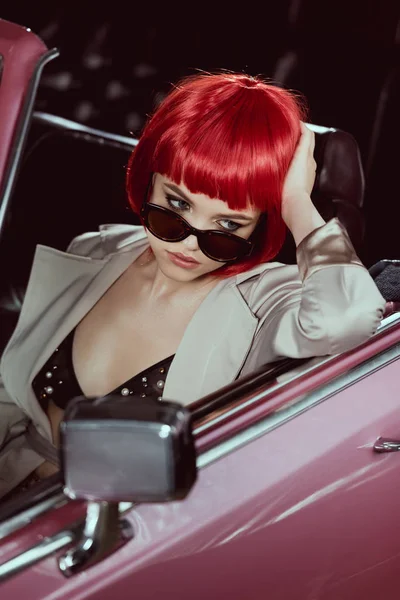 Скучающая девушка в пальто и солнцезащитных очках сидит в машине и смотрит в сторону — стоковое фото