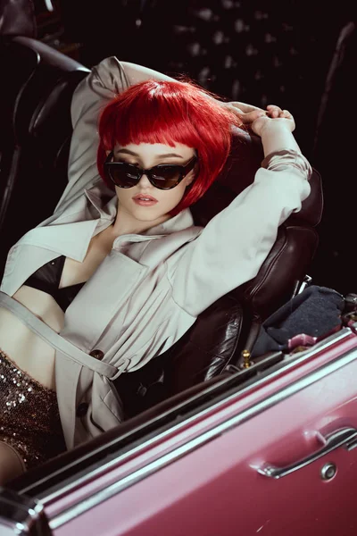 Vue grand angle de fille élégante en trench coat et lunettes de soleil assis dans la voiture rétro — Photo de stock