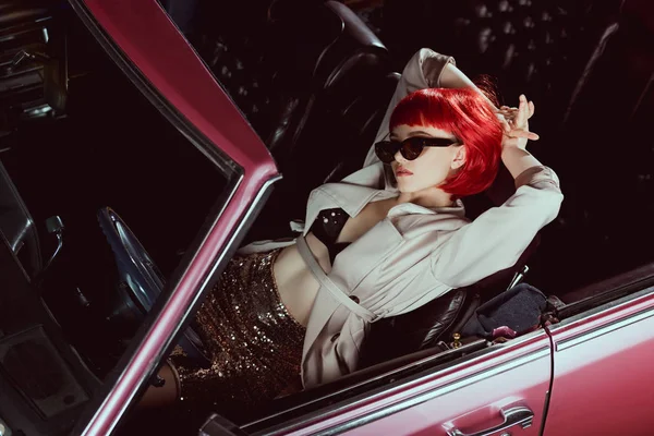 High angle view of stylish girl in trench coat and sunglasses lying with hands behind head in retro car — Stock Photo