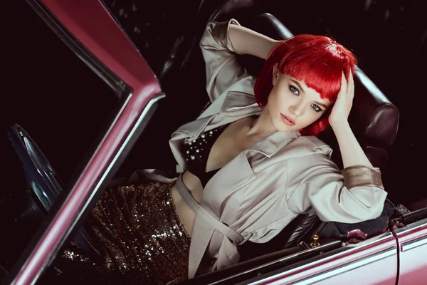 Высокий угол обзора красивой стильной молодой женщины, сидящей в классическом автомобиле и смотрящей в камеру — стоковое фото