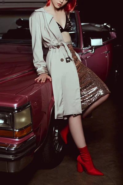 Recortado disparo de chica atractiva en abrigo de trinchera con estilo apoyado en un coche vintage - foto de stock