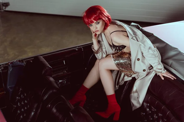 High angle view of stylish girl in trench coat looking at camera while sitting on classic car — Stock Photo