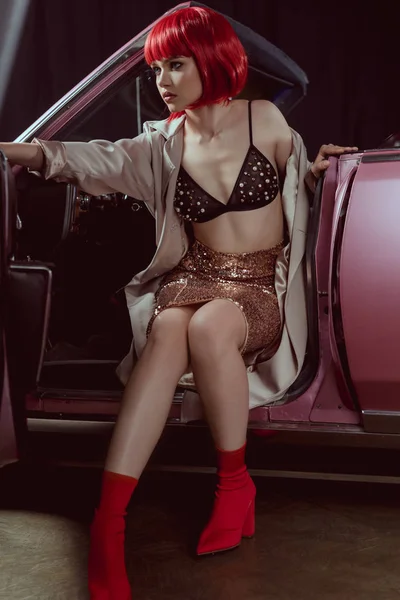 Beautiful young woman in glittering skirt and bra looking away while sitting in retro car — Stock Photo