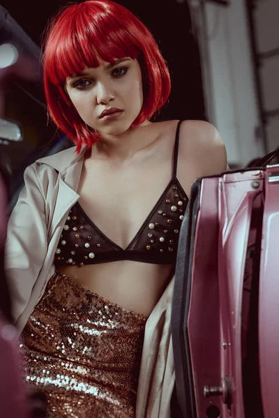 Beautiful young woman in fashionable trench coat looking at camera while sitting in retro car — Stock Photo