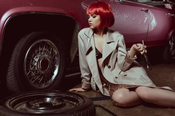 Красивая молодая женщина в плаще с гаечным ключом и ремонтом автомобиля — стоковое фото