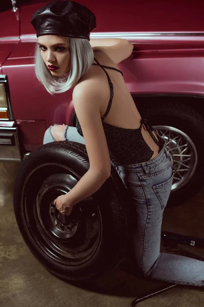 Bella ragazza bionda elegante in cuoio berretto riparazione ruota auto — Foto stock