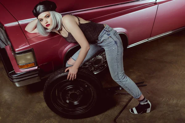 Vue grand angle de jeune femme sensuelle regardant la caméra tout en réparant la roue de voiture — Photo de stock