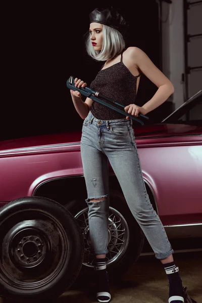 Full length view of stylish blonde woman in beret looking away while changing car wheel — Stock Photo