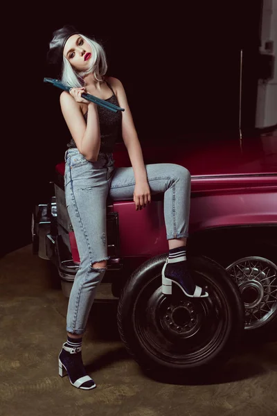 Модная блондинка, сидящая на машине и смотрящая в камеру, меняя колесо — стоковое фото
