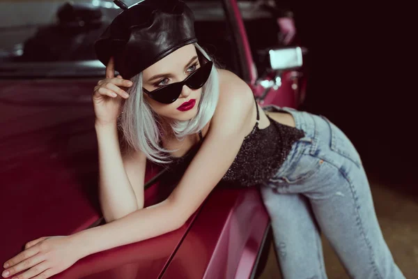 Schöne modische blonde Frau mit Sonnenbrille und schwarzer Baskenmütze lehnt am Auto und schaut weg — Stockfoto