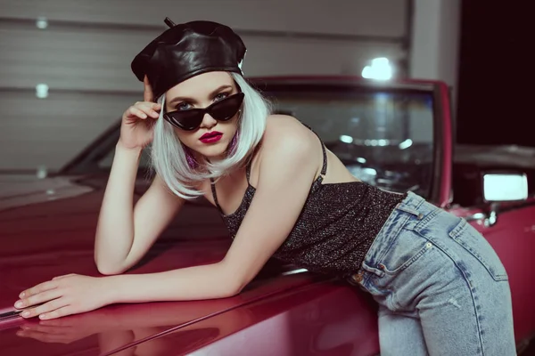 Beautiful fashionable blonde girl in beret and sunglasses leaning at retro car and looking at camera — Stock Photo