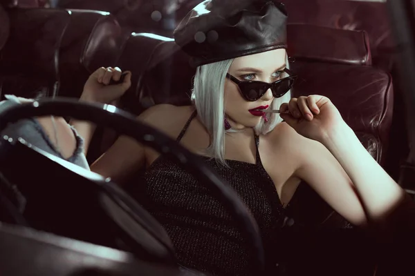 Belle fille blonde élégante tenant cigarette et regardant loin tout en étant assis dans la voiture — Photo de stock