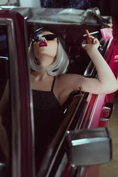 Mulher loira elegante em óculos de sol e boina fumar cigarro enquanto sentado no carro retro — Fotografia de Stock