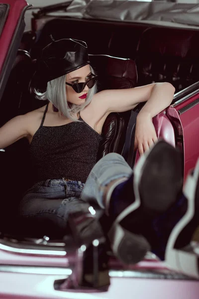 Vista de alto ângulo de menina loira elegante na boina e óculos de sol olhando para longe enquanto sentado no carro retro — Fotografia de Stock