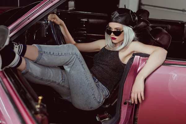 Chica rubia de moda en gafas de sol y boina sentado en coche retro - foto de stock