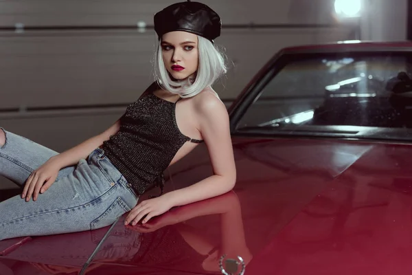 Schöne stylische junge Frau in schwarzer Baskenmütze lehnt an kastanienbraunem Auto und schaut weg — Stockfoto