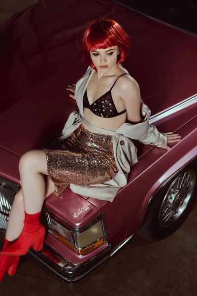High angle view of beautiful stylish girl in red wig sitting on classic car — Stock Photo