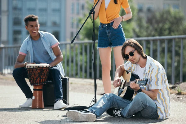 Músicos callejeros jóvenes y felices tocando música y cantando en la ciudad - foto de stock