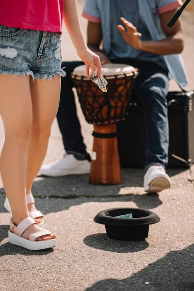 Passing by woman giving money to city street drummer playing djembe — Stock Photo