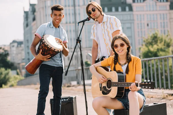 Jóvenes multirraciales tocando guitarras y djembe en la calle - foto de stock