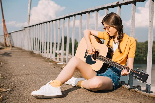 Mujer joven con guitarra sentada en el suelo y actuando en la calle - foto de stock