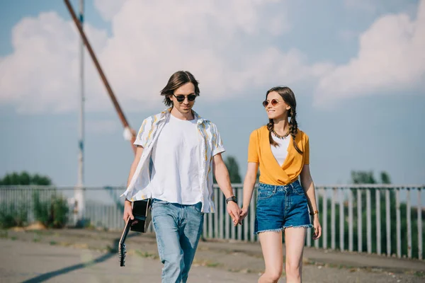 Young happy couple of buskers walking with guitar in hands at city street — Stock Photo