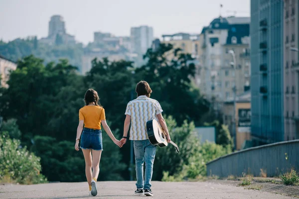 Rear view of happy street musicians walking and holding hands in city — Stock Photo