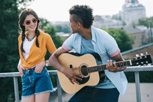 Девушка слушает африканского американского гитариста, выступающего на солнечной улице города — стоковое фото